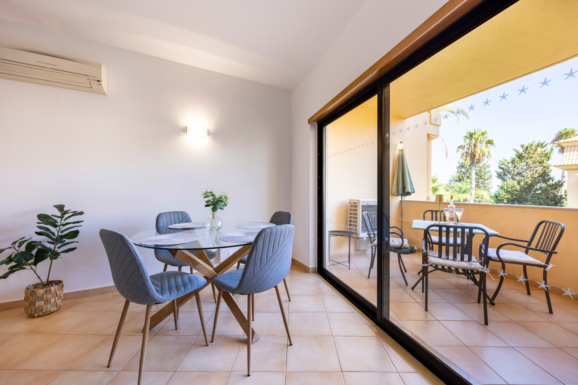 Glass dining table with four upholstered chairs beside sliding doors opening to the terrace