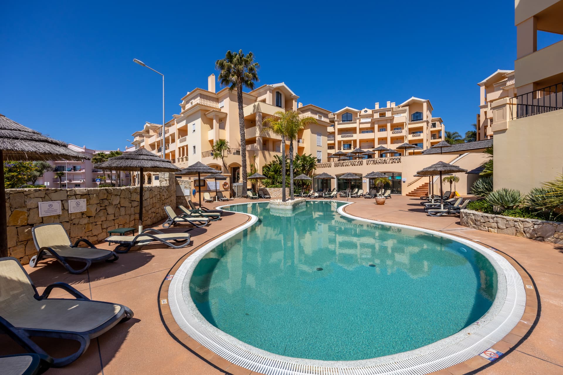 Outdoor resort pool with sun loungers, thatched parasols and palms at Estrela da Luz