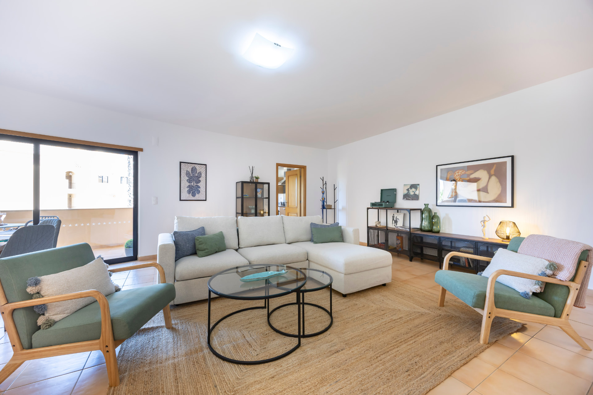 The spacious living area with a pale sectional sofa, green armchairs and glass coffee tables
