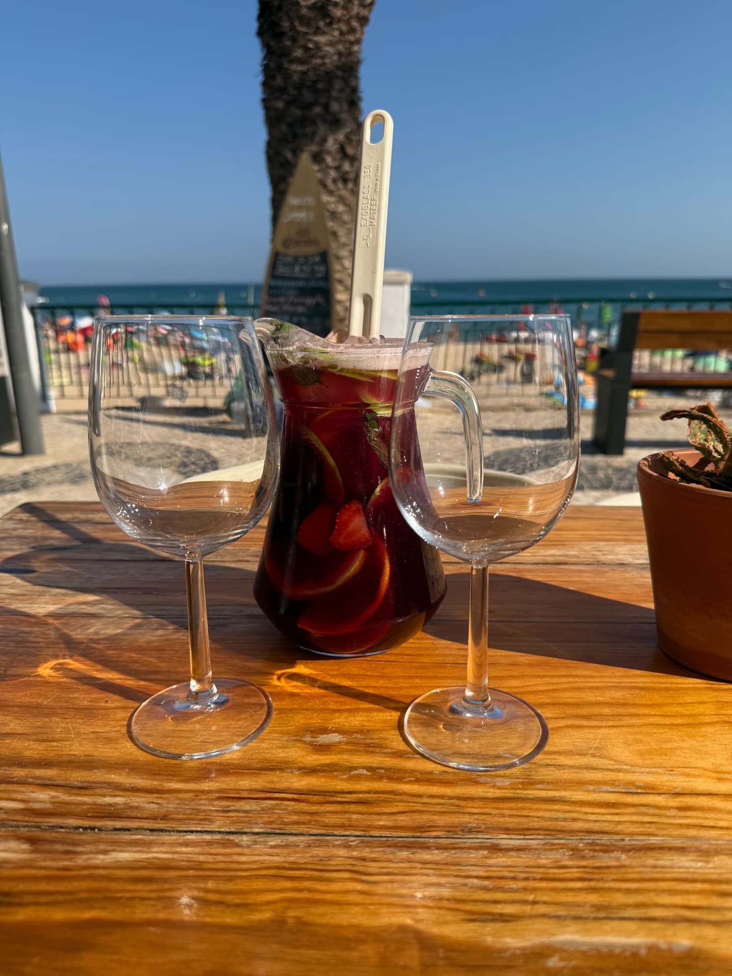 A jug of sangria and two glasses on a sunlit wooden table at a beachfront café in Luz